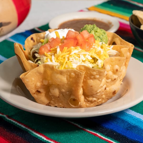 A taco salad in a crispy fried tortilla bowl, topped with cheese, tomatoes, sour cream, and guacamole.