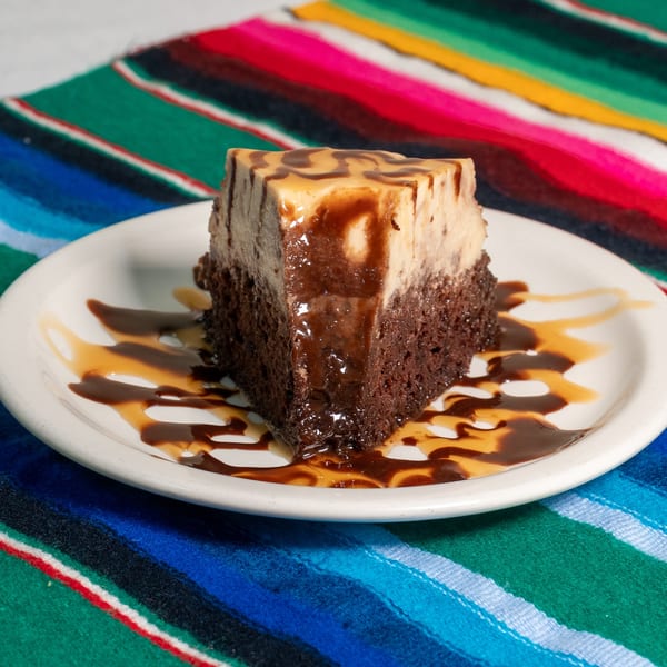 A slice of chocolate cake with flan on top, drizzled with chocolate and caramel sauce.