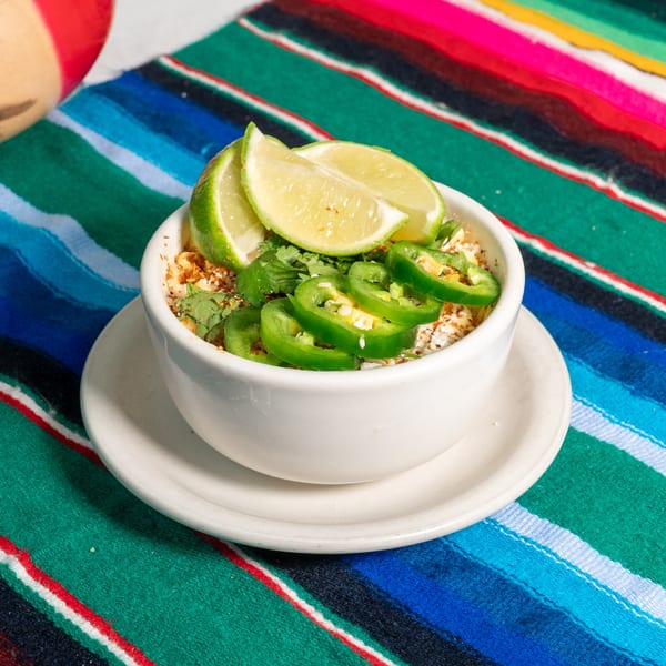 El Coronado Restaurant's esquites in a white bowl, topped with lime, jalapeños, and cilantro on a colorful serape.
