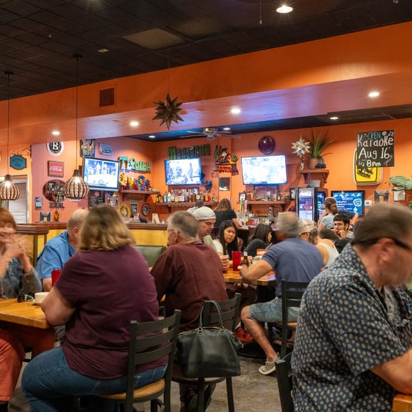 Diners seated at tables and a bar in the vibrant, orange-walled interior of El Coronado Restaurant.