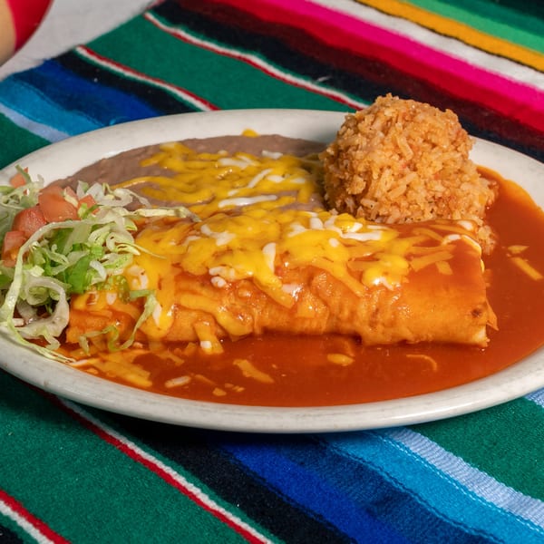 A cheesy enchilada with red sauce, rice, refried beans, and fresh salad on a colorful Mexican blanket.