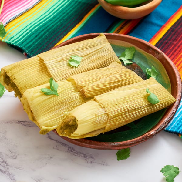 Four green tamales with cilantro on a brown plate, with a colorful striped cloth.