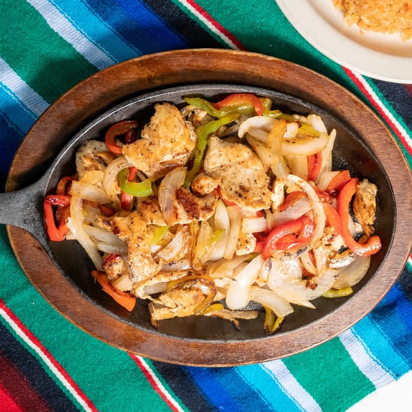 Sizzling chicken fajitas with onions and bell peppers in a cast iron skillet on a colorful Mexican blanket.